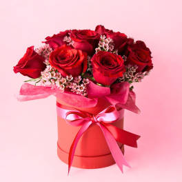 Red roses arranged in a pink hat box with a ribbon bow