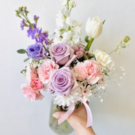 Handheld bouquet of pastel roses, carnations, tulips, and white blooms in a glass vase