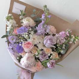 Pastel bouquet of roses, peonies, and lavender flowers wrapped in brown paper
