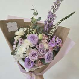 Hand-tied bouquet of lavender, white, and pink flowers wrapped in brown paper
