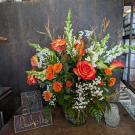 Orange and red roses in a glass vase with white filler flowers