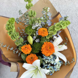 Bouquet of orange marigolds, white lilies, and blue flowers wrapped in brown paper