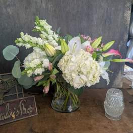 White lilies and hydrangeas in a glass vase with pink accents