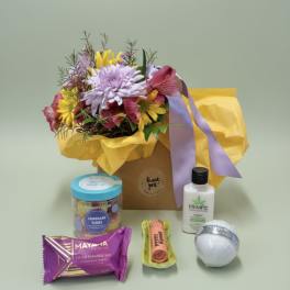 Mixed flower bouquet in a gift bag with assorted treats and a lotion bottle