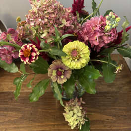 Mixed bouquet with pink hydrangeas, zinnias, and yellow blooms in a glass vase