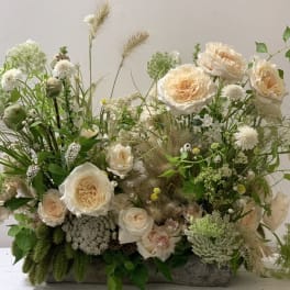 Cream roses and wildflowers arranged in a low rustic container