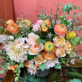 Mixed bouquet of peach, pink, and cream flowers in a dark container