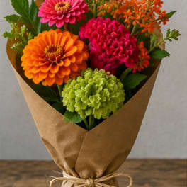 Bright mixed bouquet of zinnias and small orange flowers wrapped in brown paper