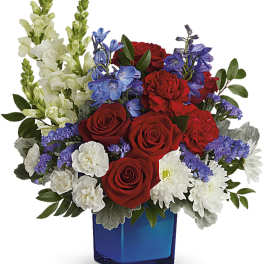 Red roses, white snapdragons, and purple flowers in a blue glass vase
