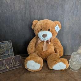 Brown teddy bear with a ribbon sitting beside a glass candle holder