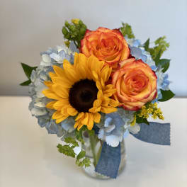 Bouquet of sunflowers, orange roses, and blue hydrangeas in a glass vase
