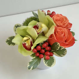 Compact bouquet with orange roses, green orchids, and red berries in a white vase