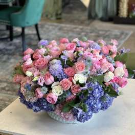 Large pastel bouquet of pink roses and blue hydrangeas in a white bowl vase