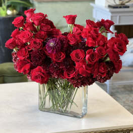 Red roses and dark purple blooms arranged in a clear rectangular vase