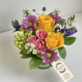 Bouquet of yellow and pink roses with purple daisies in a glass vase