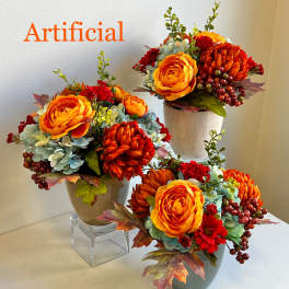 Three artificial floral arrangements in small vases with orange and red blooms
