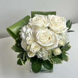 White rose bouquet in a clear square vase with green foliage