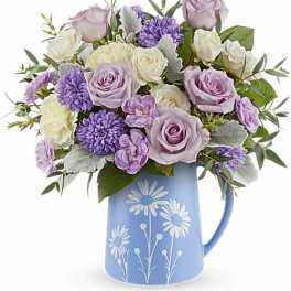 Lavender roses and purple flowers in a blue pitcher vase