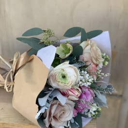 Hand-tied bouquet of pale roses and mixed blooms wrapped in kraft paper