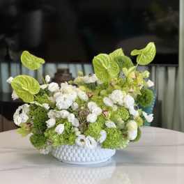 Green and white floral arrangement in a white textured bowl vase