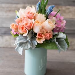 Peach and pink roses in a pale blue vase with blue grape hyacinths