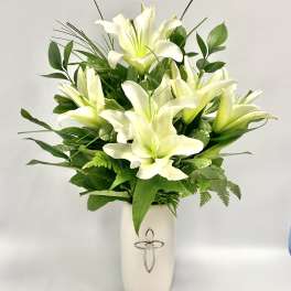 White lilies arranged in a white vase with green foliage