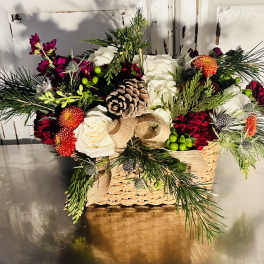 Holiday floral arrangement in a woven basket with pinecones and white roses