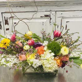 Mixed bouquet in a low rectangular glass vase with pink, yellow, white, and orange blooms