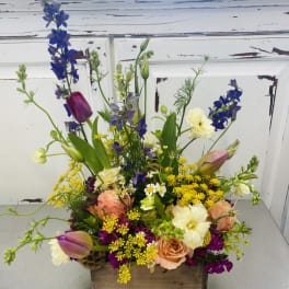 Mixed bouquet in a wooden box with tulips, roses, and blue delphinium
