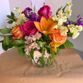 Mixed bouquet of roses, lilies, and purple blooms in a glass vase