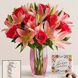 Pink lilies and red roses in a tall glass vase with a card and chocolates