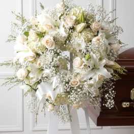 White floral funeral spray on a stand beside a casket