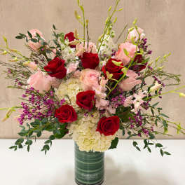 Red and blush roses in a tall green vase with white hydrangeas