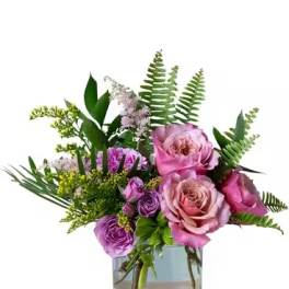 Pink and purple roses in a clear glass vase with fern foliage