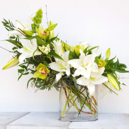 White lilies and green orchids in a clear glass vase
