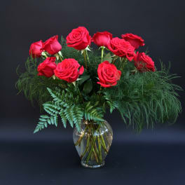 Red roses arranged in a clear glass vase with airy greenery