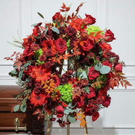 Large red floral wreath on a stand beside a casket