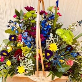 Large basket arrangement of multicolored flowers with a wooden handle