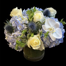 Blue hydrangeas with white roses and orchids in a glass vase