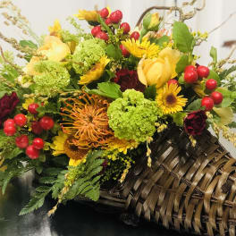 Mixed bouquet with yellow roses, red berries, and green blooms in a woven basket