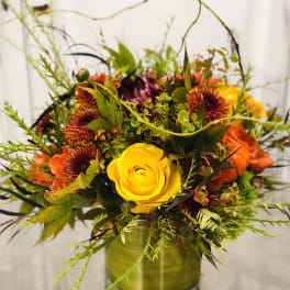 Yellow rose arrangement with orange and burgundy flowers in a glass vase