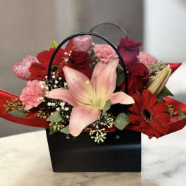 Red and pink flower arrangement in a black handled gift box