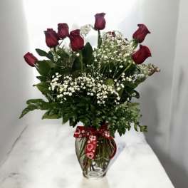 Red roses in a glass vase with baby's breath and a heart ribbon