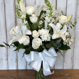 White lilies and roses arranged in a glass vase with a white ribbon