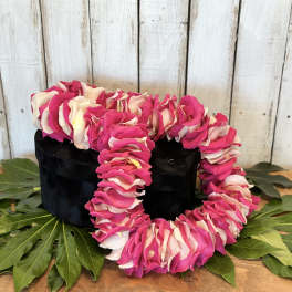 Pink and white flower lei draped over a black box on green leaves
