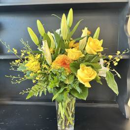 Yellow roses and lilies arranged in a clear glass vase
