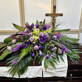 Purple and green floral casket spray with a crucifix behind it