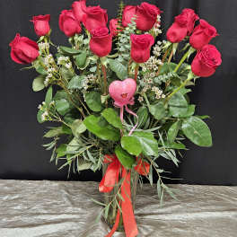 Bouquet of red roses with greenery in a clear glass vase and pink heart pick
