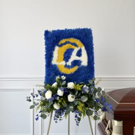 Blue and yellow floral funeral tribute on an easel beside a casket