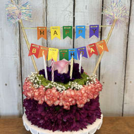 Birthday cake decorated with flowers and a colorful HAPPY BIRTHDAY banner